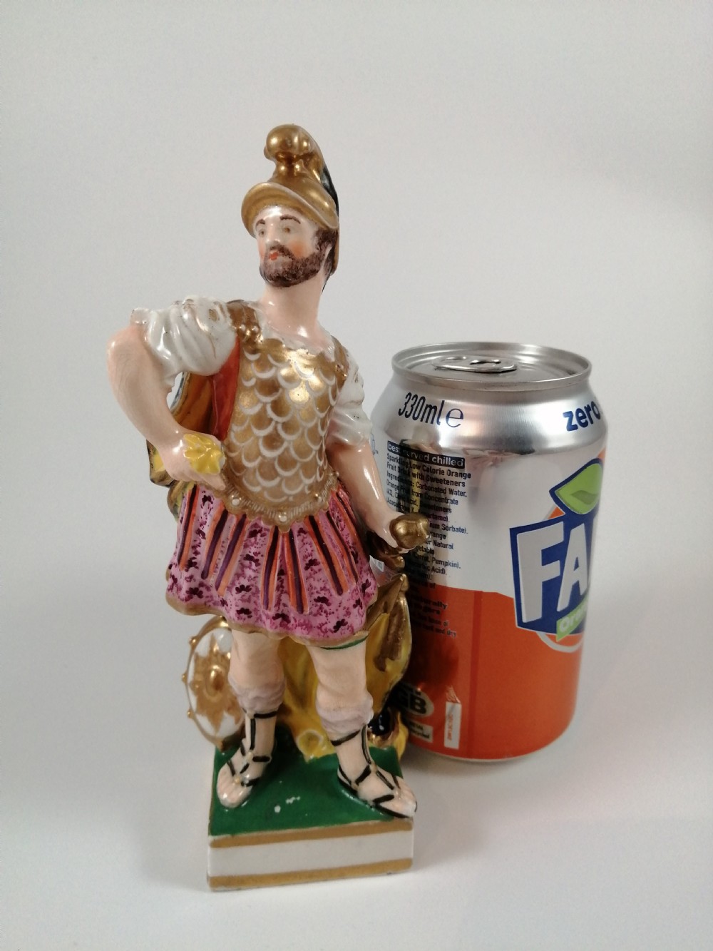 An antique hand-painted porcelain figure depicting the Roman god Mars in gilded armour, a pink tunic, and a golden helmet, standing on a green base. View XV