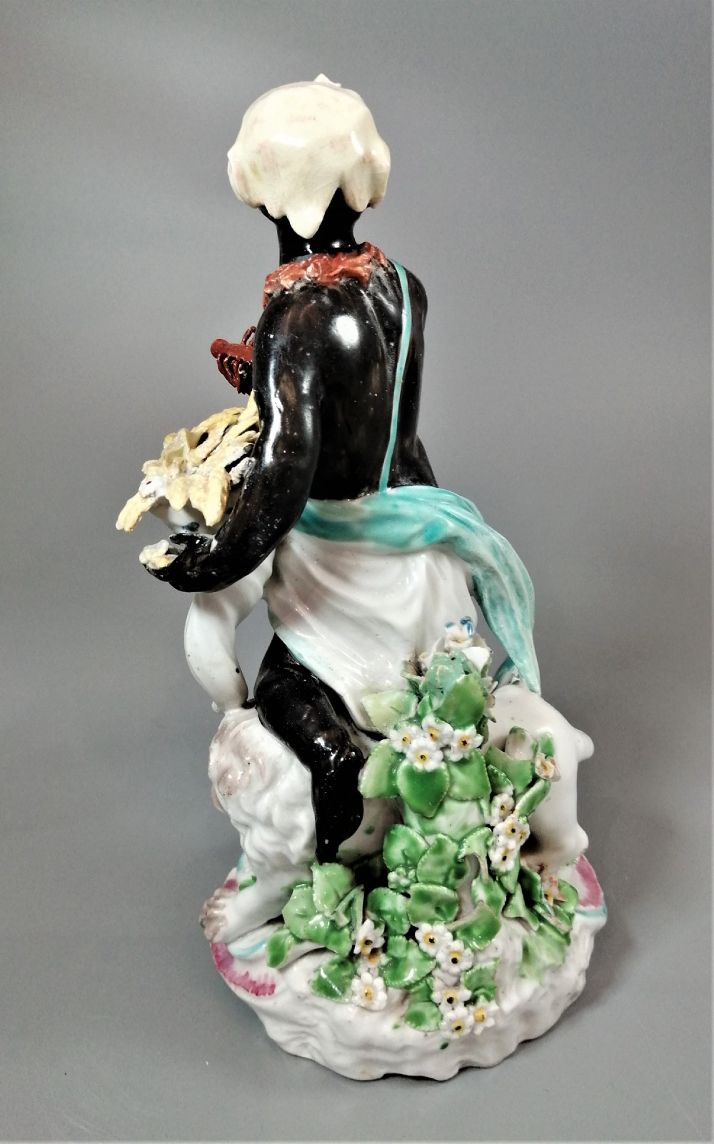 An 18th-century Derby soft-paste porcelain figurine depicting an allegorical figure of Africa wearing an elephant scalp headdress beside a crouching lion on a rococo scroll base. View IV