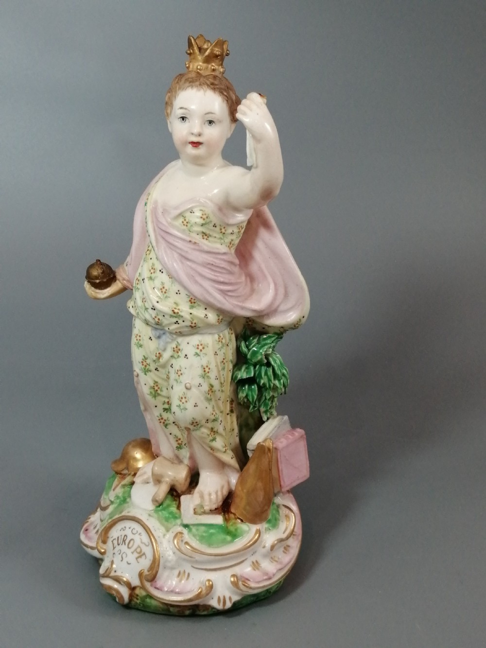 An 18th-century Derby soft-paste porcelain statuette representing Europe, featuring a crowned figure in patterned drapery standing on a gilded scrollwork base.