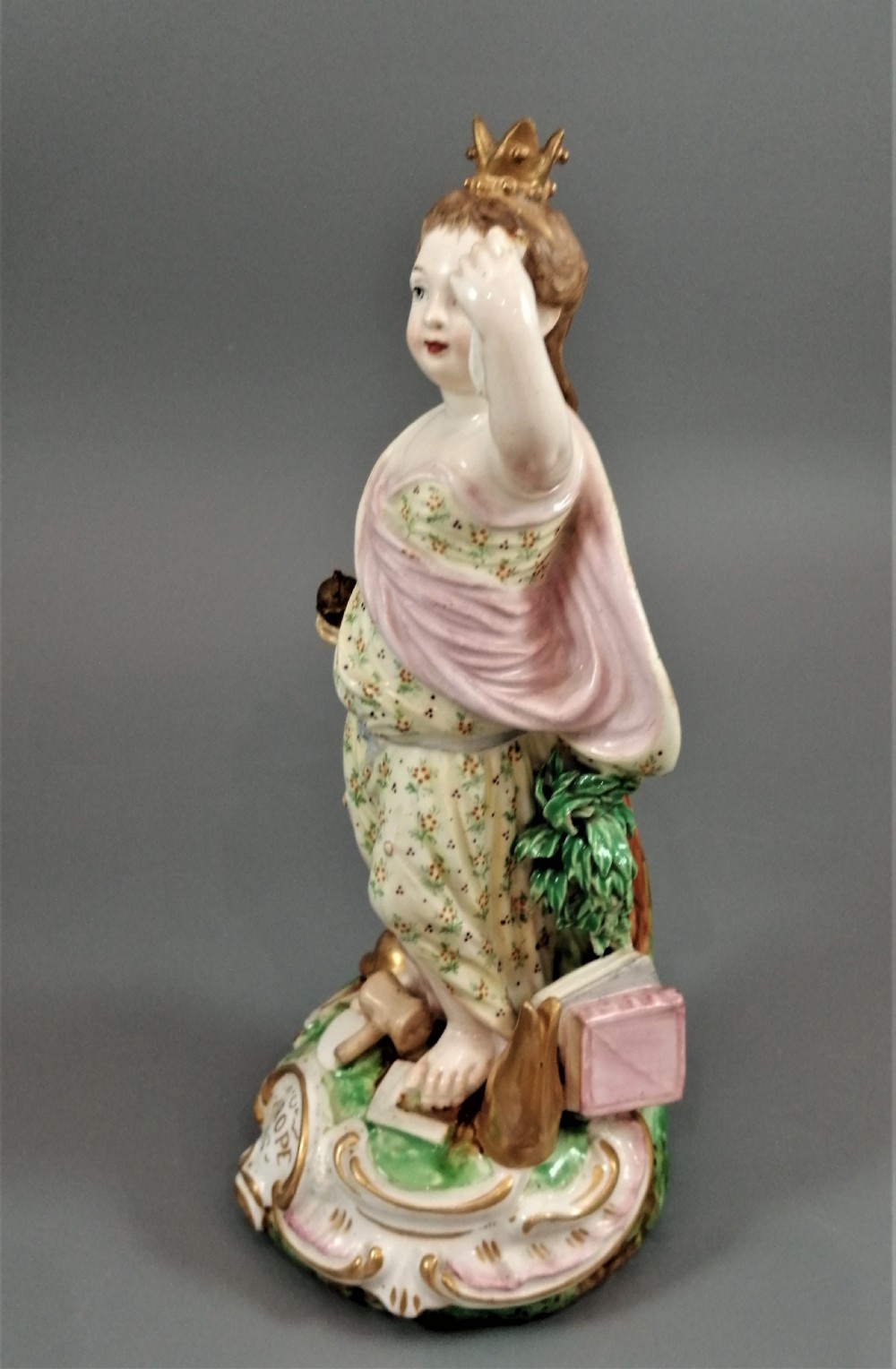 An 18th-century Derby soft-paste porcelain statuette representing Europe, featuring a crowned figure in patterned drapery standing on a gilded scrollwork base. View IV