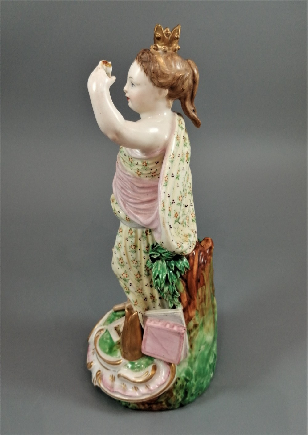 An 18th-century Derby soft-paste porcelain statuette representing Europe, featuring a crowned figure in patterned drapery standing on a gilded scrollwork base. View V