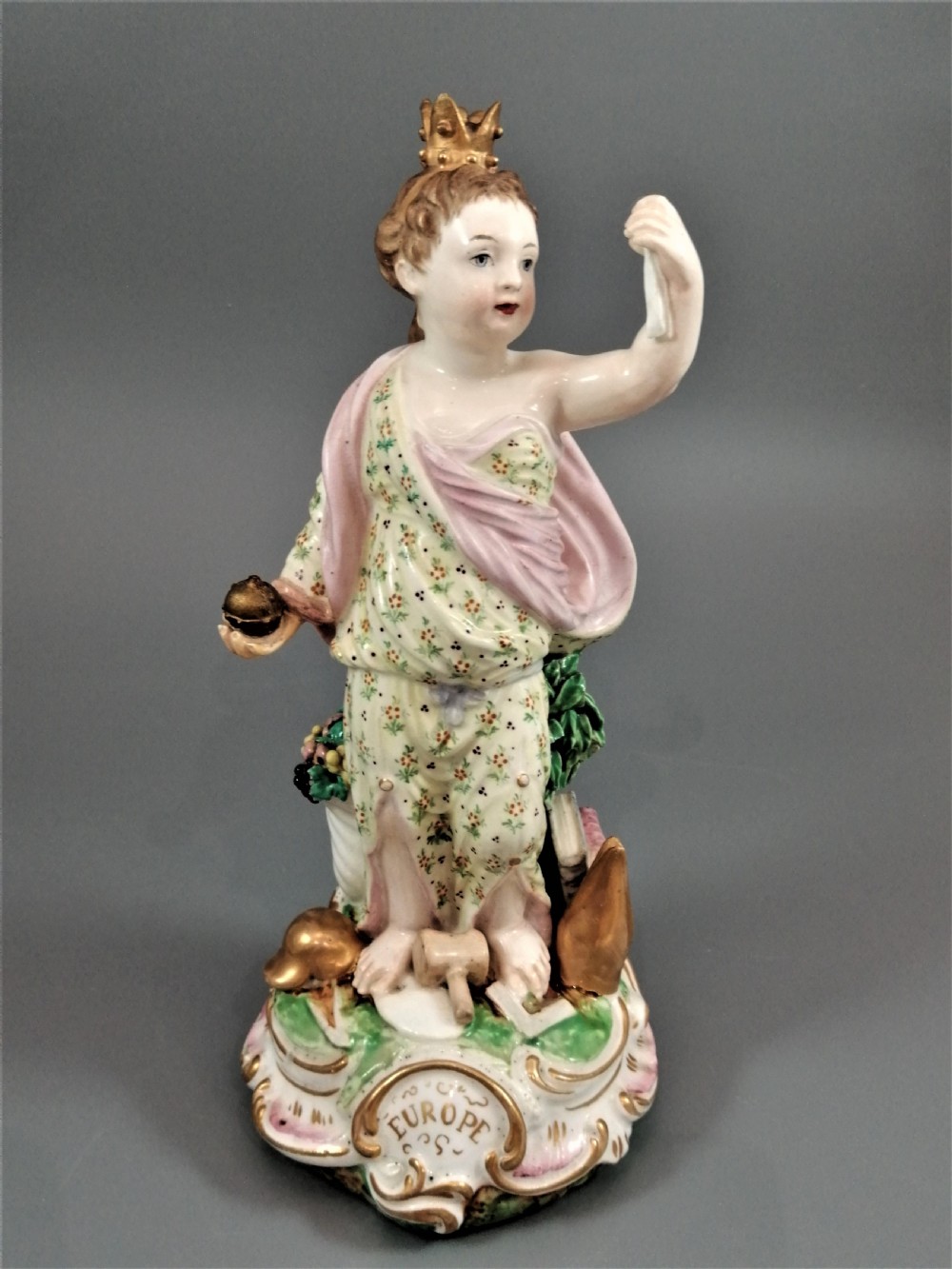 An 18th-century Derby soft-paste porcelain statuette representing Europe, featuring a crowned figure in patterned drapery standing on a gilded scrollwork base. View VIII