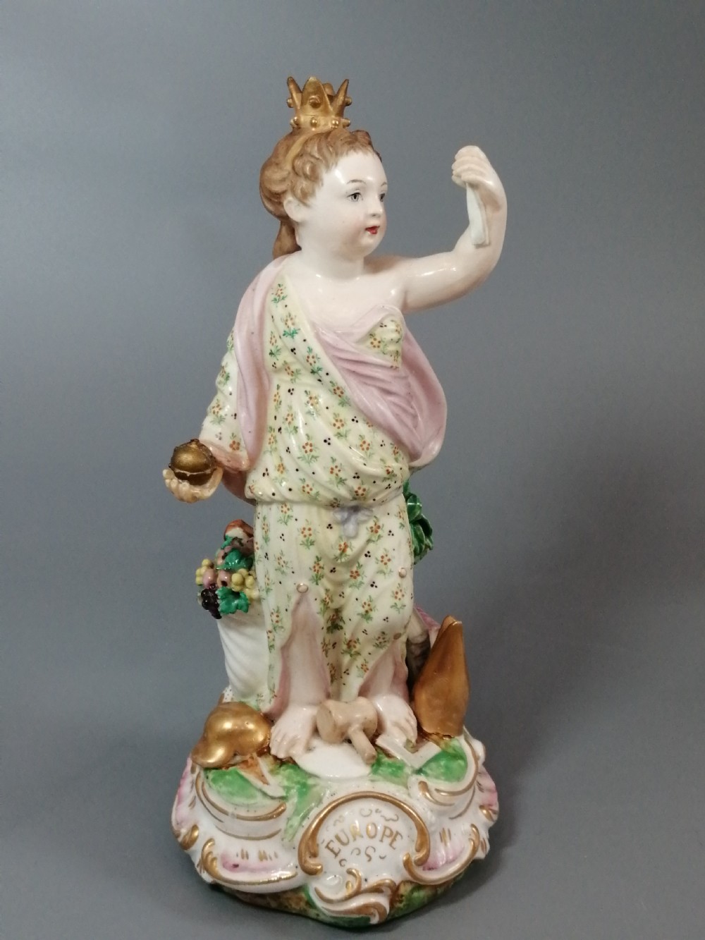 An 18th-century Derby soft-paste porcelain statuette representing Europe, featuring a crowned figure in patterned drapery standing on a gilded scrollwork base. View XI
