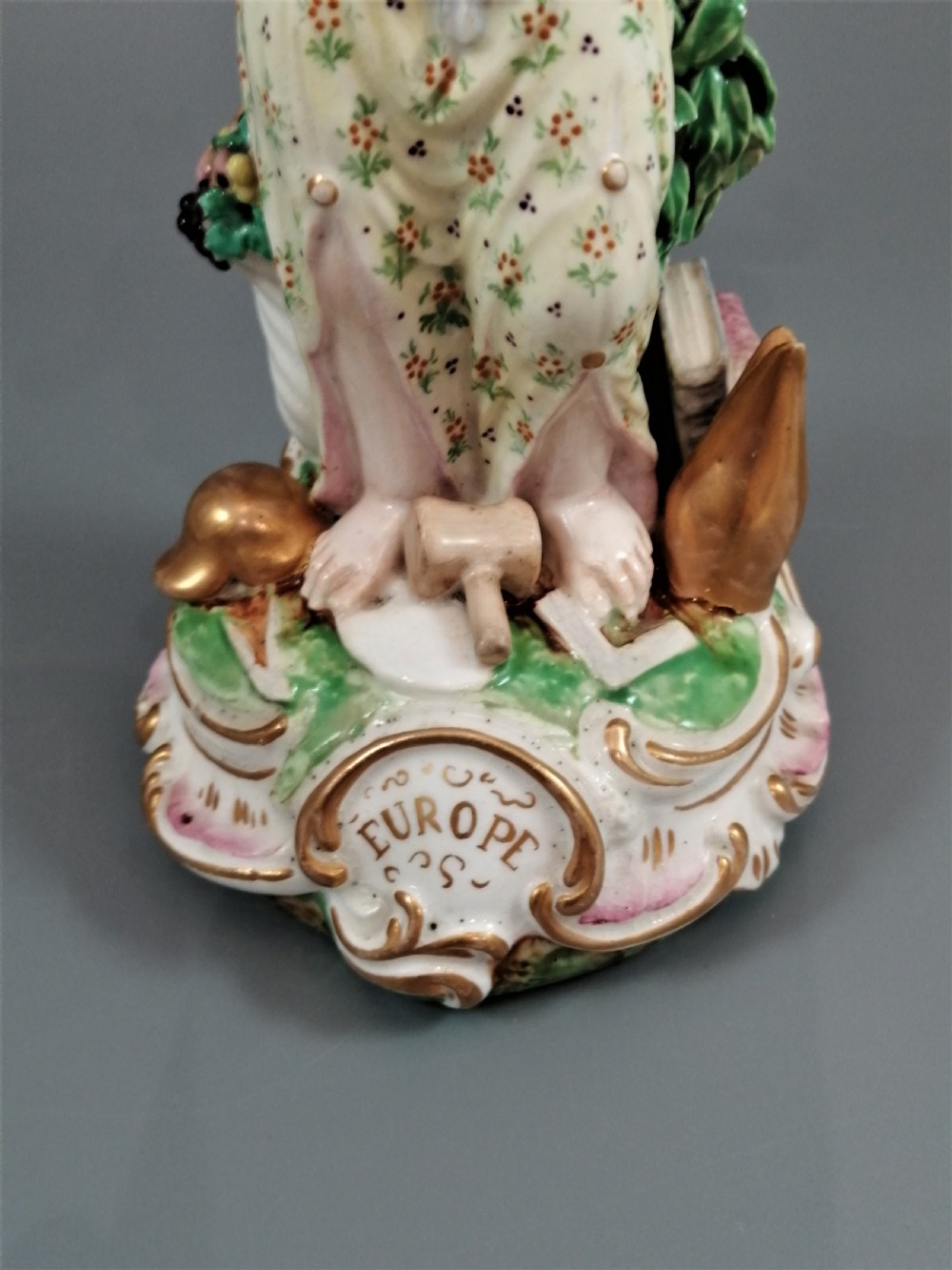 An 18th-century Derby soft-paste porcelain statuette representing Europe, featuring a crowned figure in patterned drapery standing on a gilded scrollwork base. View XII