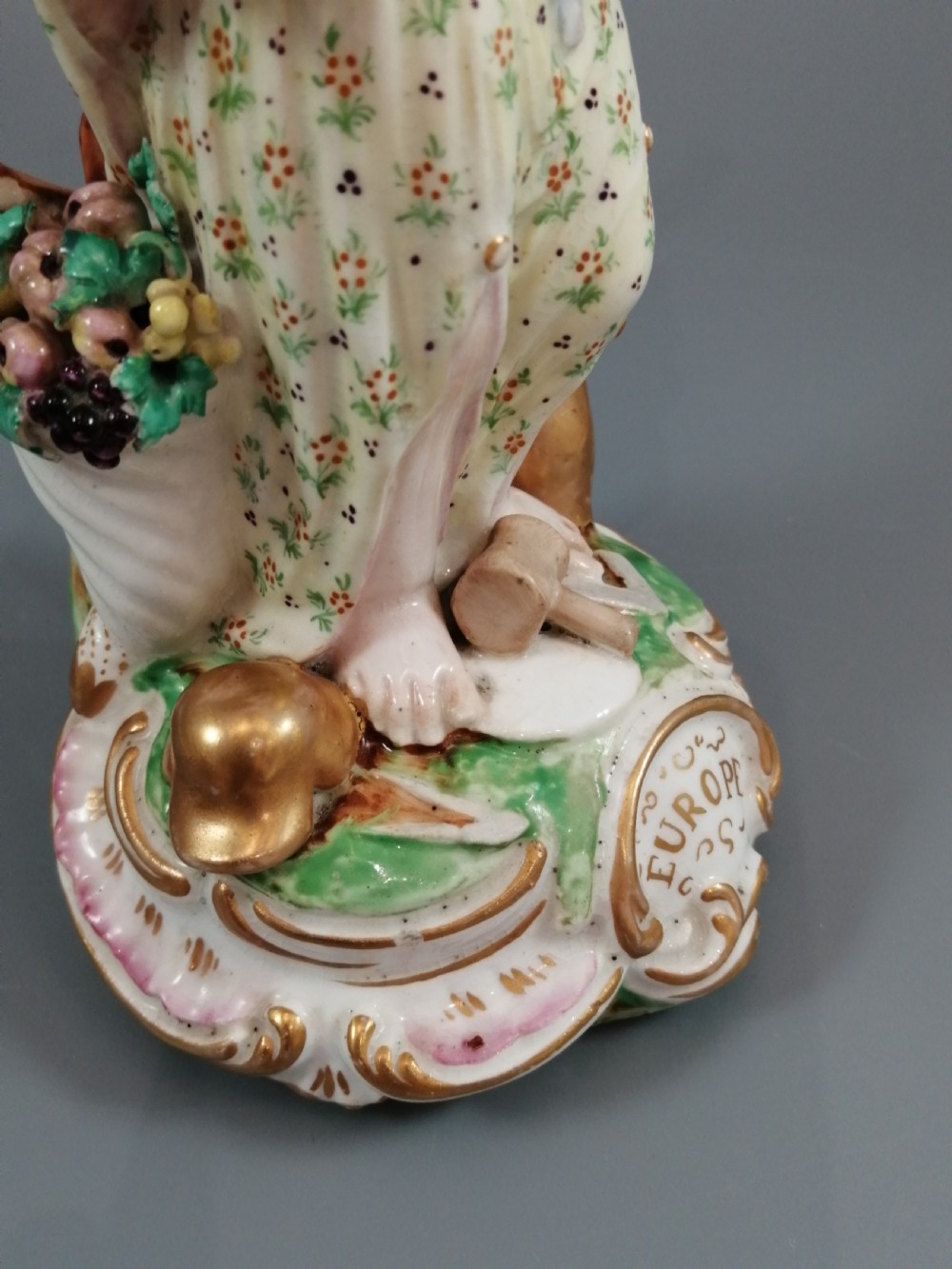 An 18th-century Derby soft-paste porcelain statuette representing Europe, featuring a crowned figure in patterned drapery standing on a gilded scrollwork base. View XIII