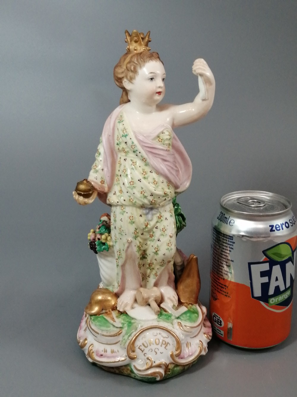 An 18th-century Derby soft-paste porcelain statuette representing Europe, featuring a crowned figure in patterned drapery standing on a gilded scrollwork base. View XVI