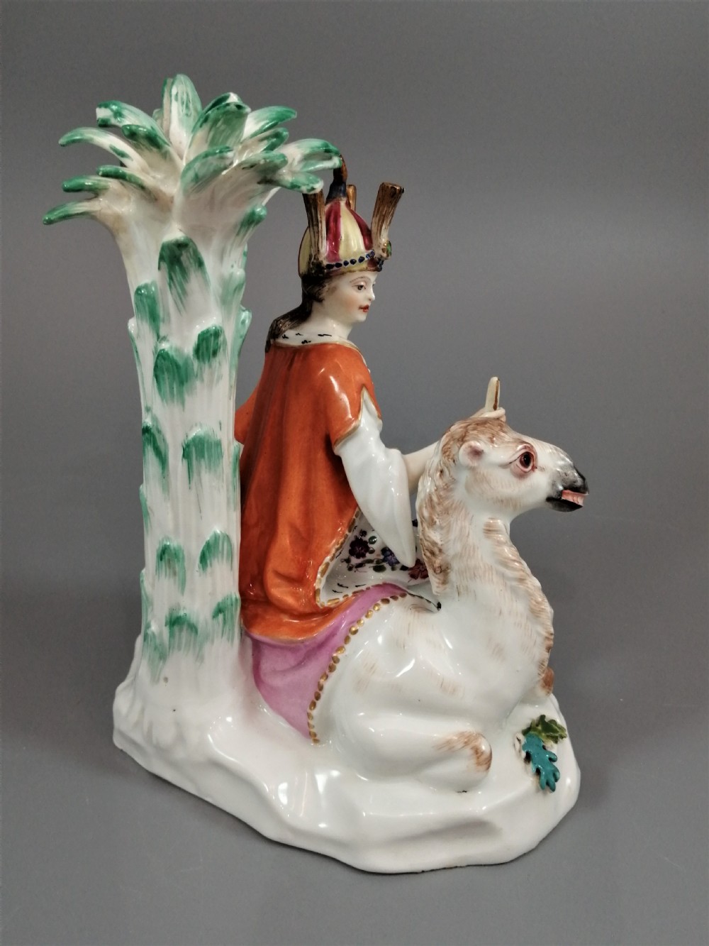 An 18th-century Chelsea soft-paste porcelain figurine depicting an allegorical female figure of Asia seated beside a camel beneath a palm tree. View IV