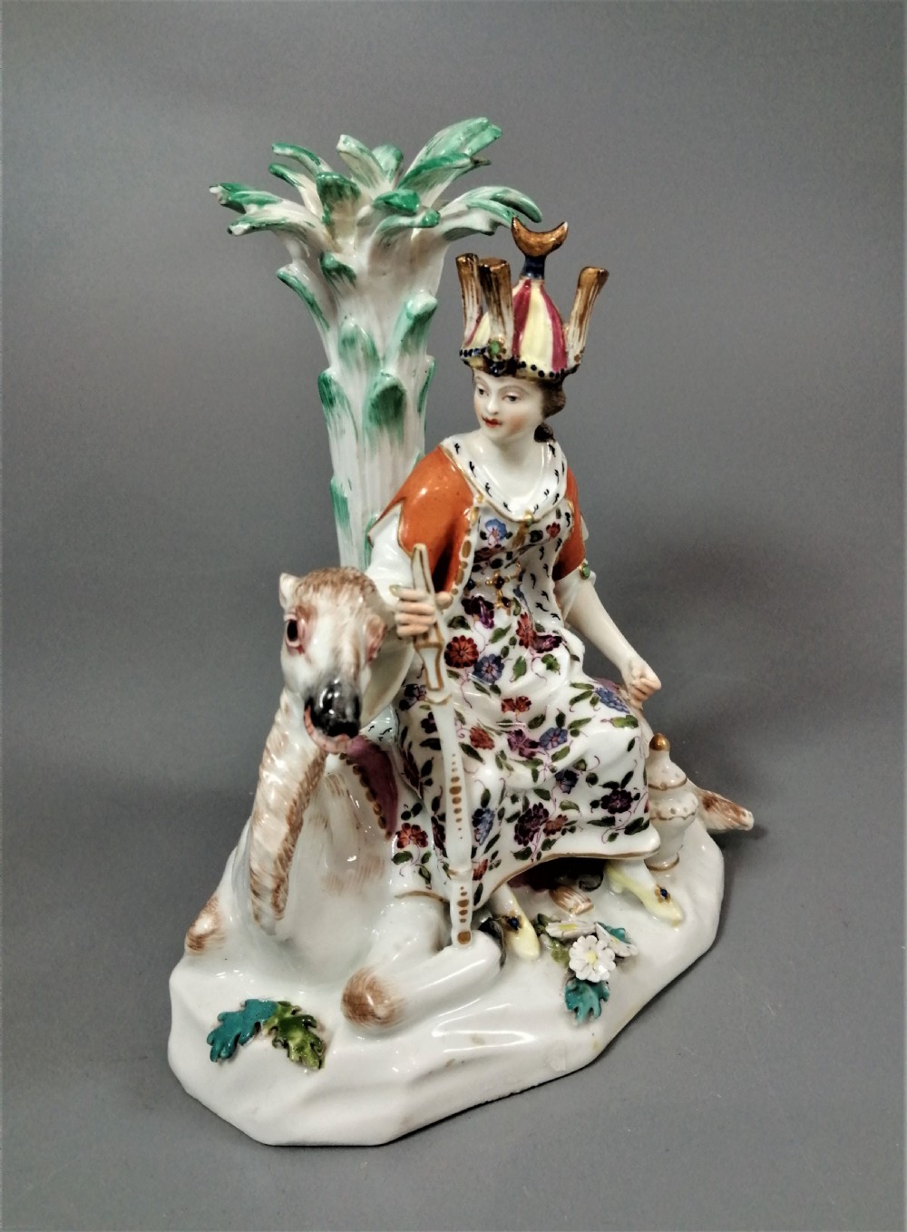 An 18th-century Chelsea soft-paste porcelain figurine depicting an allegorical female figure of Asia seated beside a camel beneath a palm tree. View V