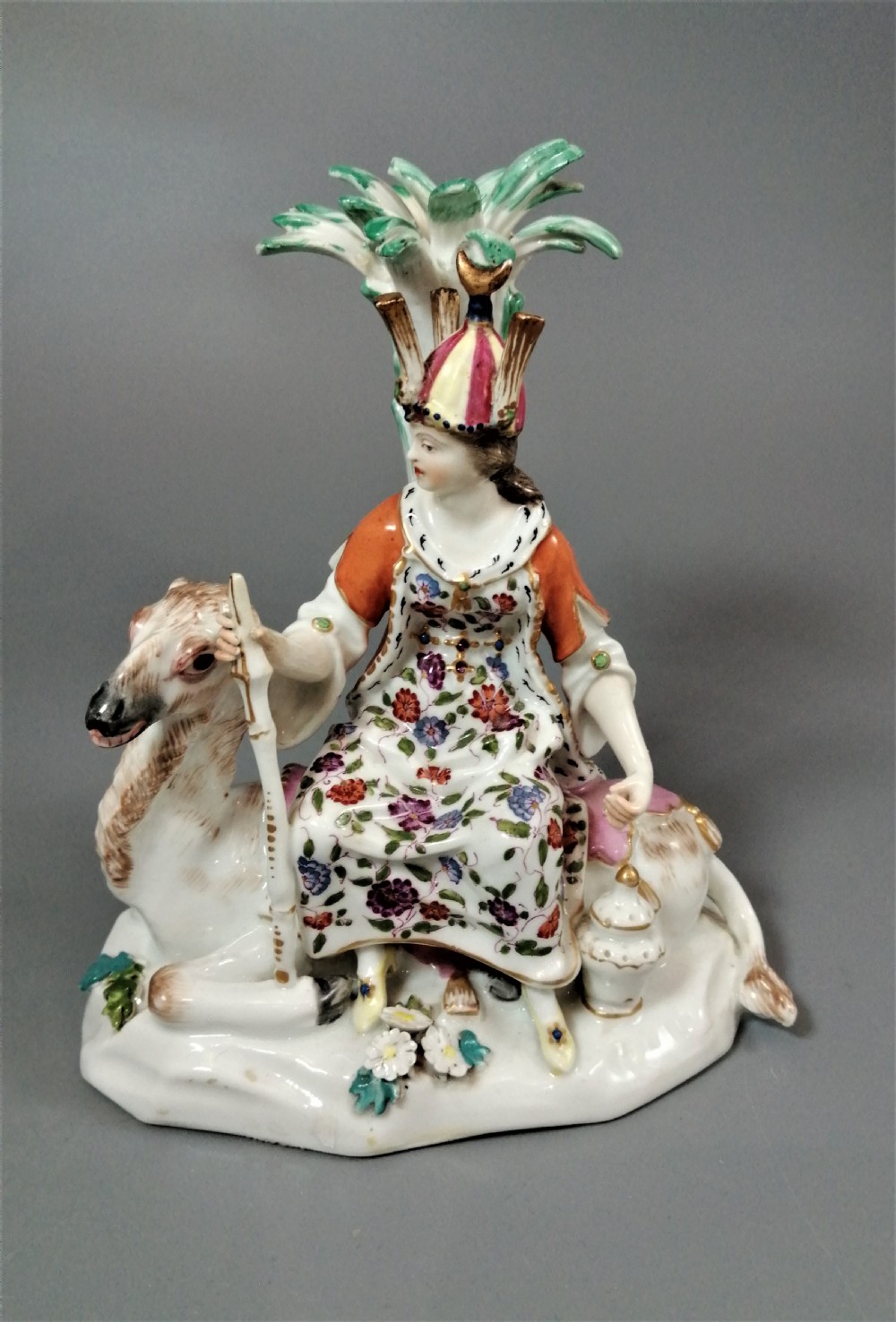 An 18th-century Chelsea soft-paste porcelain figurine depicting an allegorical female figure of Asia seated beside a camel beneath a palm tree. View VII