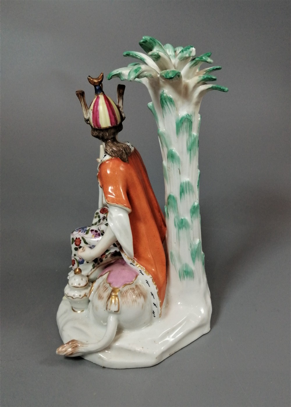 An 18th-century Chelsea soft-paste porcelain figurine depicting an allegorical female figure of Asia seated beside a camel beneath a palm tree. View VIII