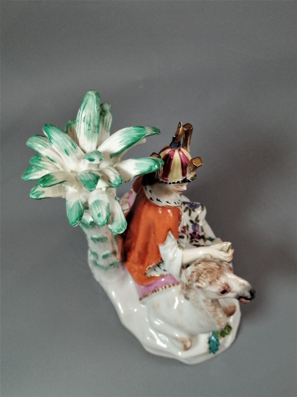 An 18th-century Chelsea soft-paste porcelain figurine depicting an allegorical female figure of Asia seated beside a camel beneath a palm tree. View X