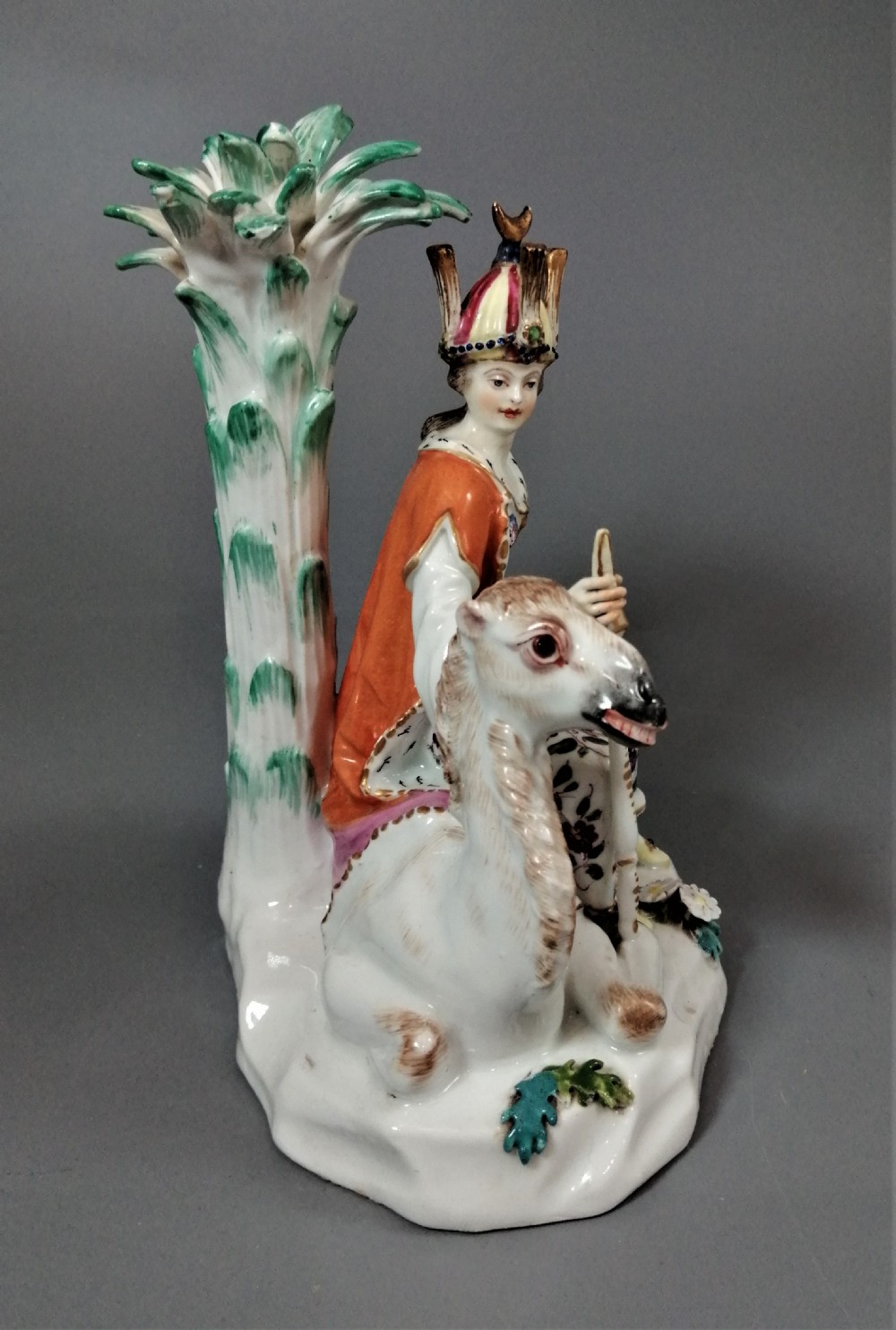 An 18th-century Chelsea soft-paste porcelain figurine depicting an allegorical female figure of Asia seated beside a camel beneath a palm tree. View XII