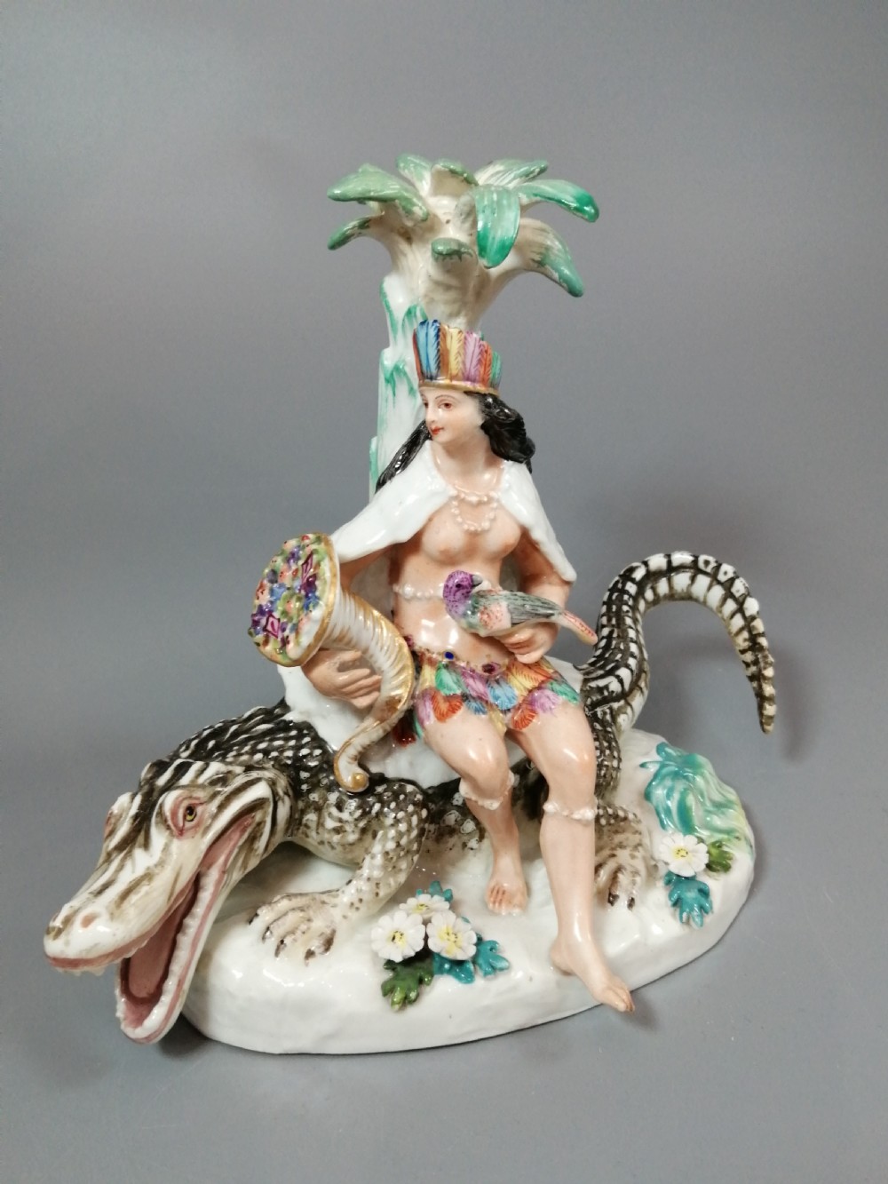 An 18th-century Chelsea polychrome porcelain statuette depicting an allegorical female figure seated on an alligator beside a palm tree.