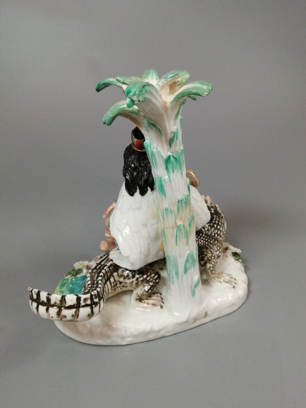 An 18th-century Chelsea polychrome porcelain statuette depicting an allegorical female figure seated on an alligator beside a palm tree. View IV