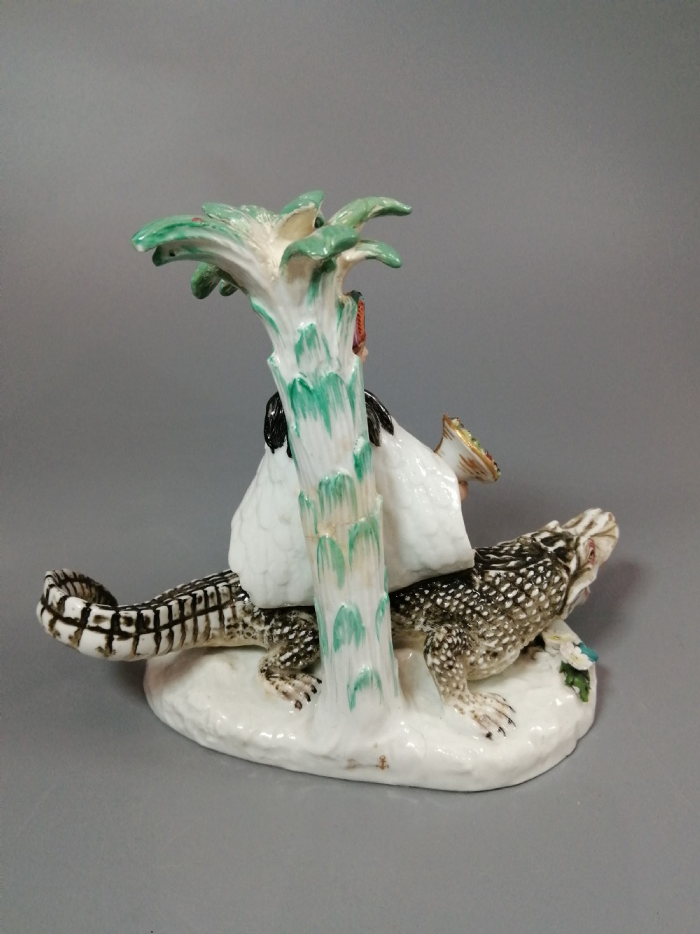 An 18th-century Chelsea polychrome porcelain statuette depicting an allegorical female figure seated on an alligator beside a palm tree. View V
