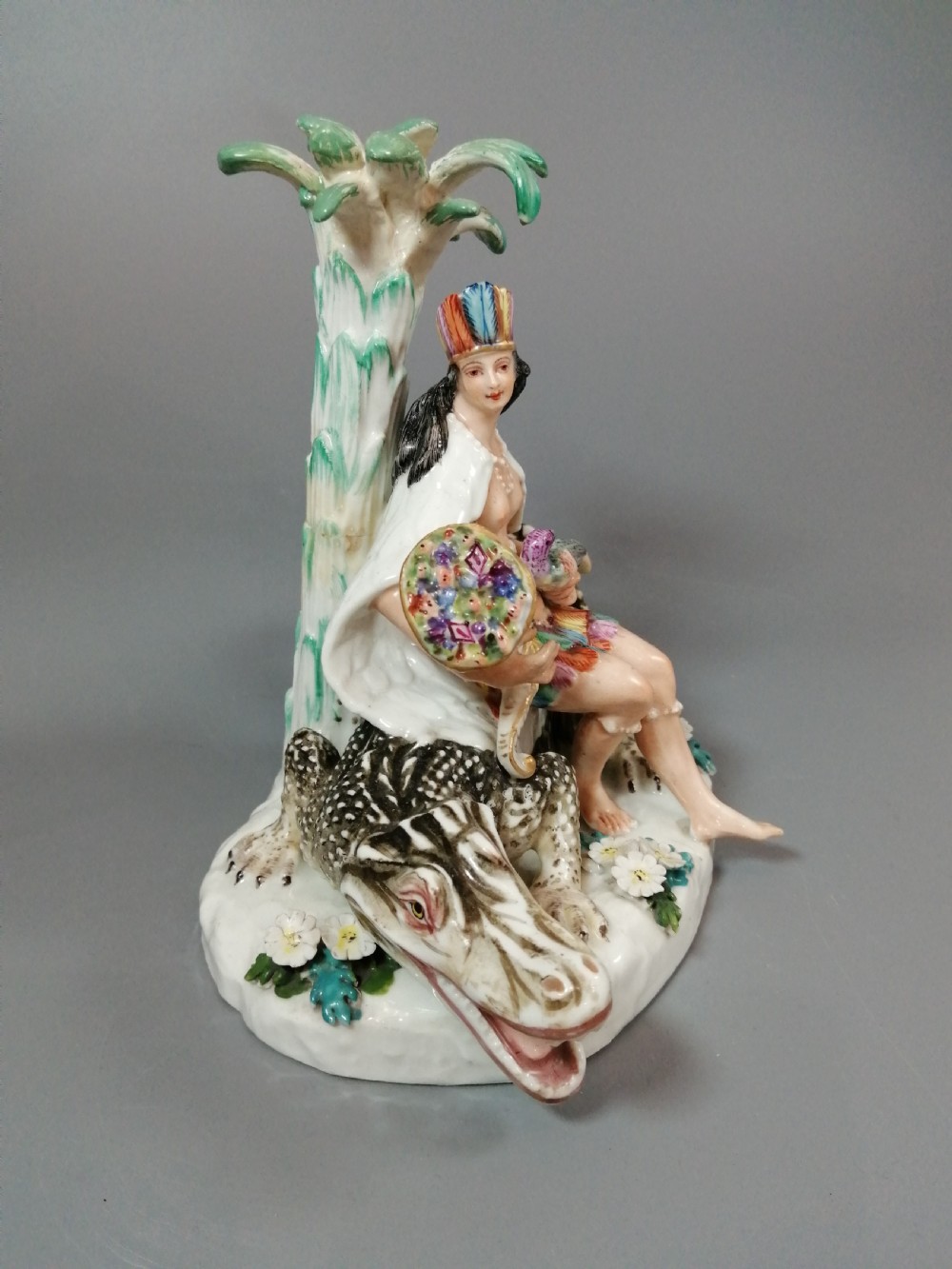 An 18th-century Chelsea polychrome porcelain statuette depicting an allegorical female figure seated on an alligator beside a palm tree. View VII