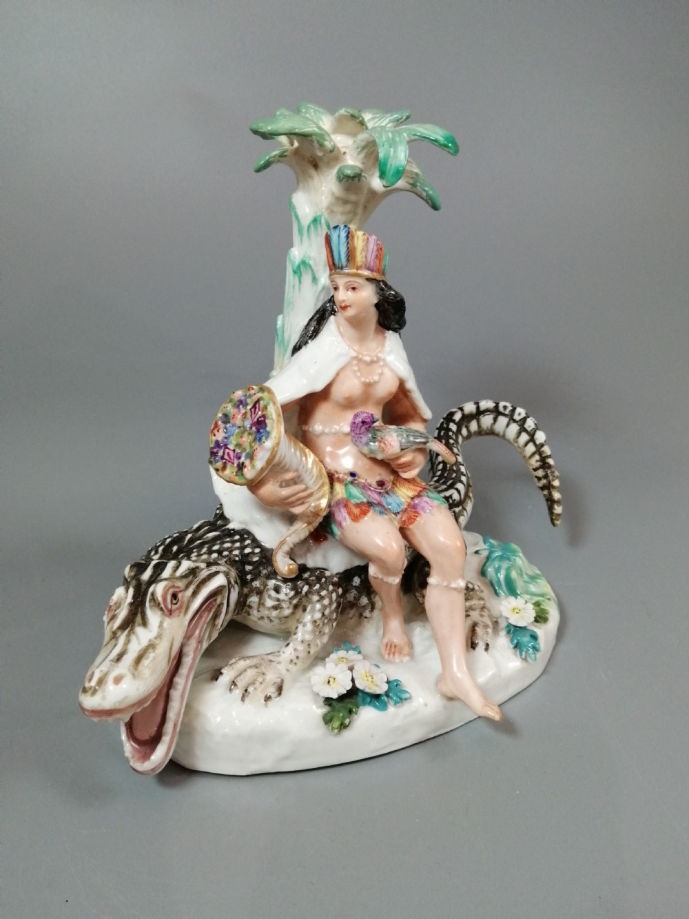 An 18th-century Chelsea polychrome porcelain statuette depicting an allegorical female figure seated on an alligator beside a palm tree. View VIII