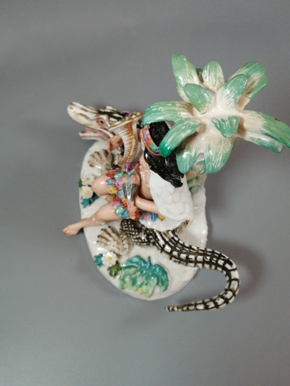 An 18th-century Chelsea polychrome porcelain statuette depicting an allegorical female figure seated on an alligator beside a palm tree. View XI
