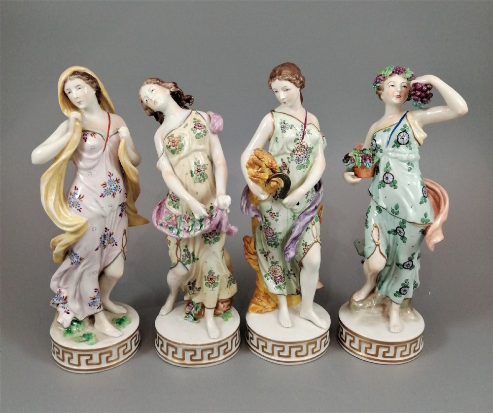 A set of four Sitzendorf polychrome glazed porcelain figurines representing allegories of the Four Seasons, standing on cylindrical Greek key patterned bases.