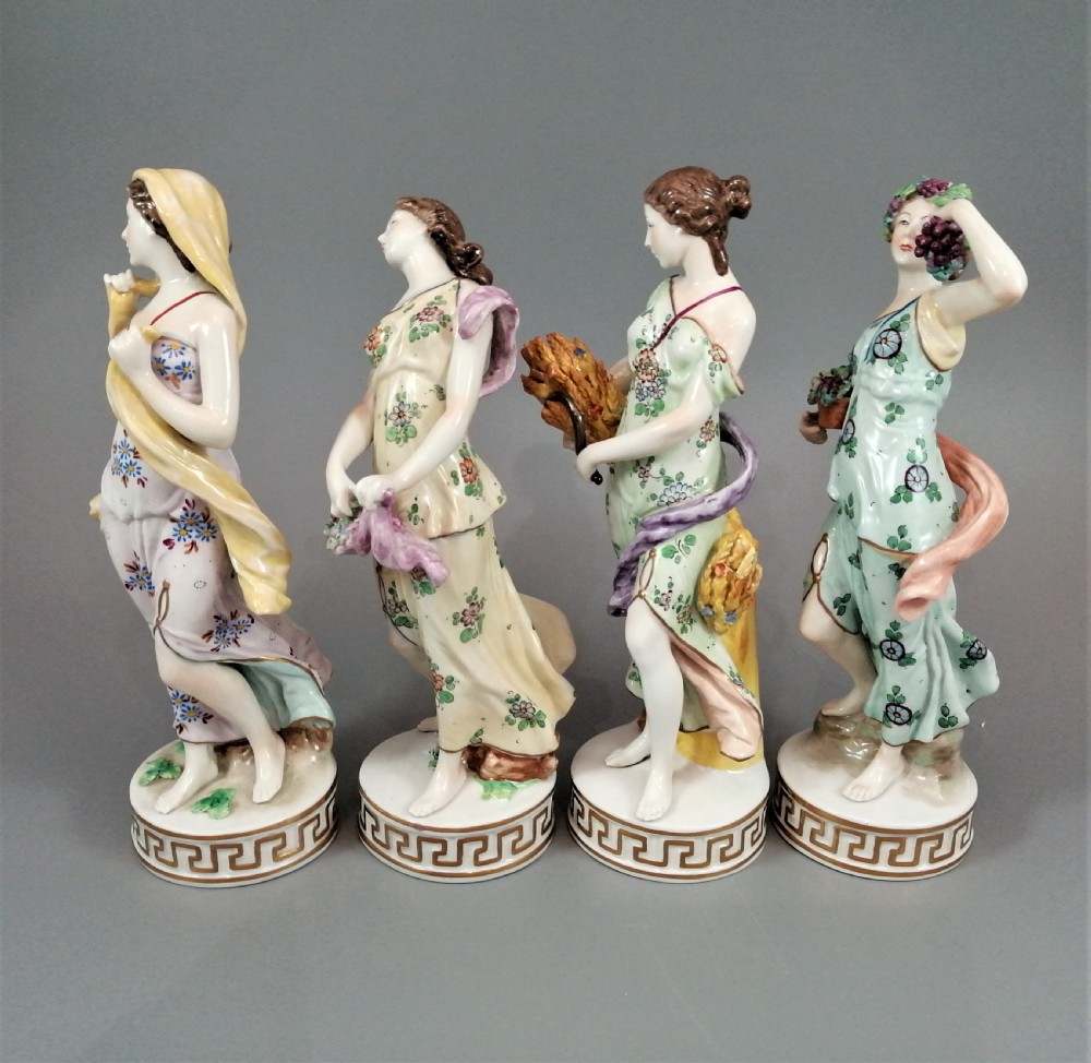 A set of four Sitzendorf polychrome glazed porcelain figurines representing allegories of the Four Seasons, standing on cylindrical Greek key patterned bases. View II