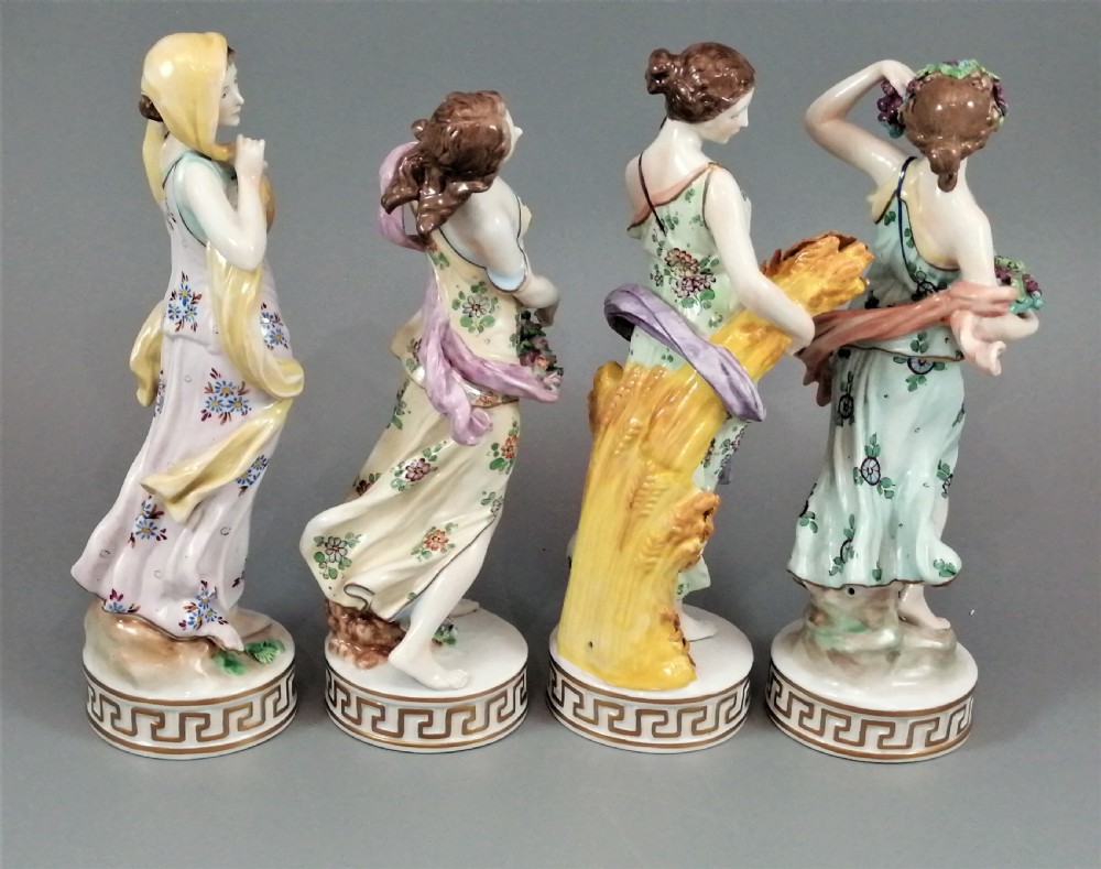 A set of four Sitzendorf polychrome glazed porcelain figurines representing allegories of the Four Seasons, standing on cylindrical Greek key patterned bases. View IV