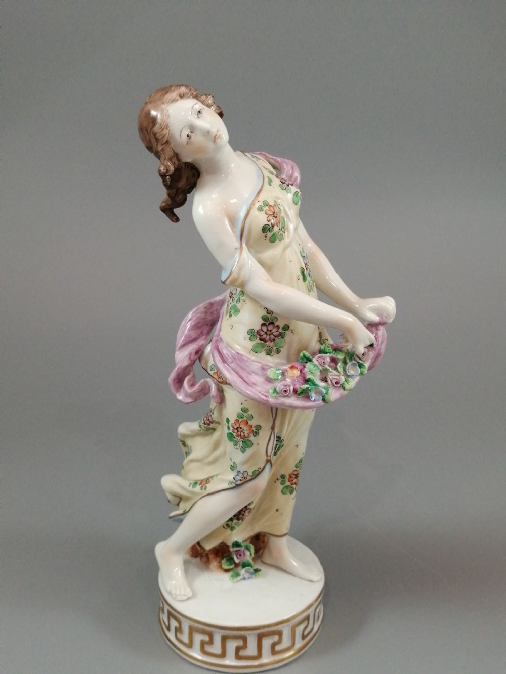 A set of four Sitzendorf polychrome glazed porcelain figurines representing allegories of the Four Seasons, standing on cylindrical Greek key patterned bases. View VI