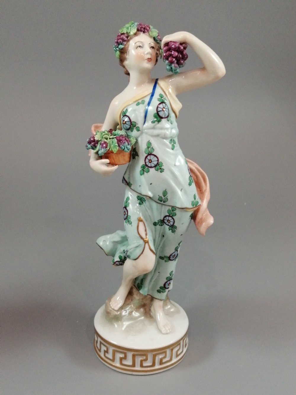 A set of four Sitzendorf polychrome glazed porcelain figurines representing allegories of the Four Seasons, standing on cylindrical Greek key patterned bases. View VIII