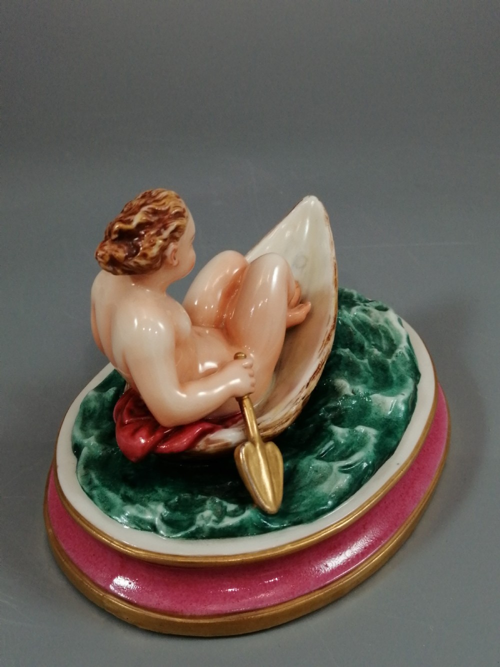 A 19th-century majolica ceramic figurine depicting a figure seated in a small boat over green waves, mounted on a pink glazed oval base with gilded borders. View VII