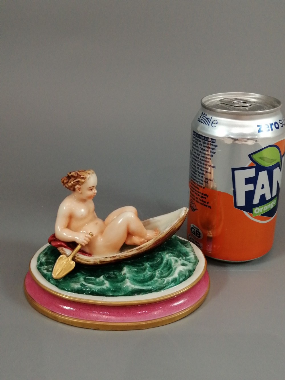A 19th-century majolica ceramic figurine depicting a figure seated in a small boat over green waves, mounted on a pink glazed oval base with gilded borders. View XII