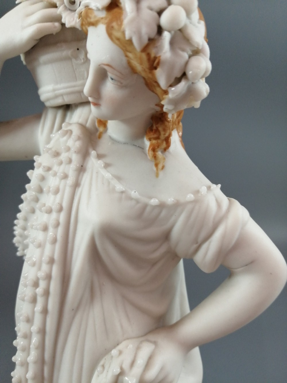 A nineteenth-century Victorian Parian ware figurine depicting a classically draped maiden holding a fruit basket on her shoulder. View VII