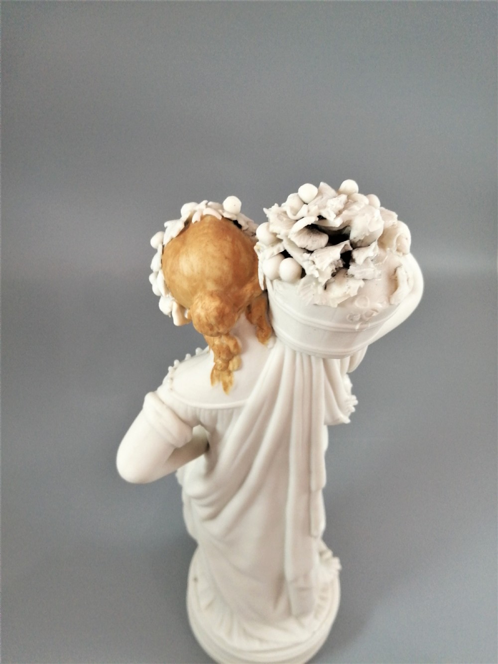 A nineteenth-century Victorian Parian ware figurine depicting a classically draped maiden holding a fruit basket on her shoulder. View XIII