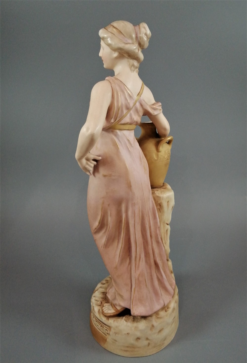 A Royal Dux porcelain statuette of a classical maiden in a draped dusty pink gown holding an earthenware jug. View III