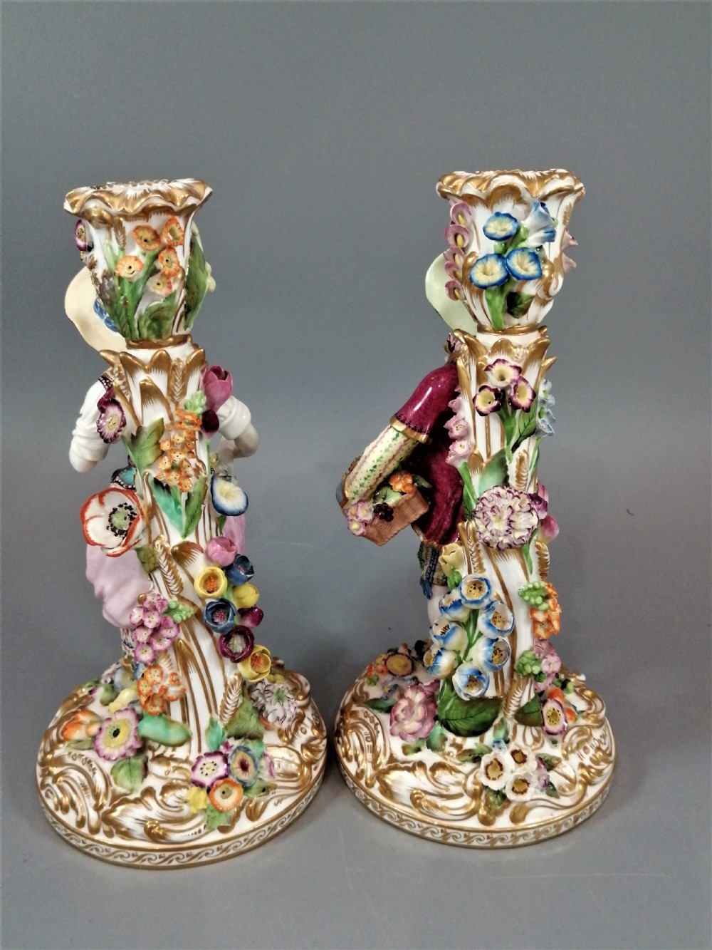 A pair of hand-painted Minton porcelain figural candlesticks featuring a male and female figure in colourful traditional dress with floral motifs and gilded scroll bases. View IV
