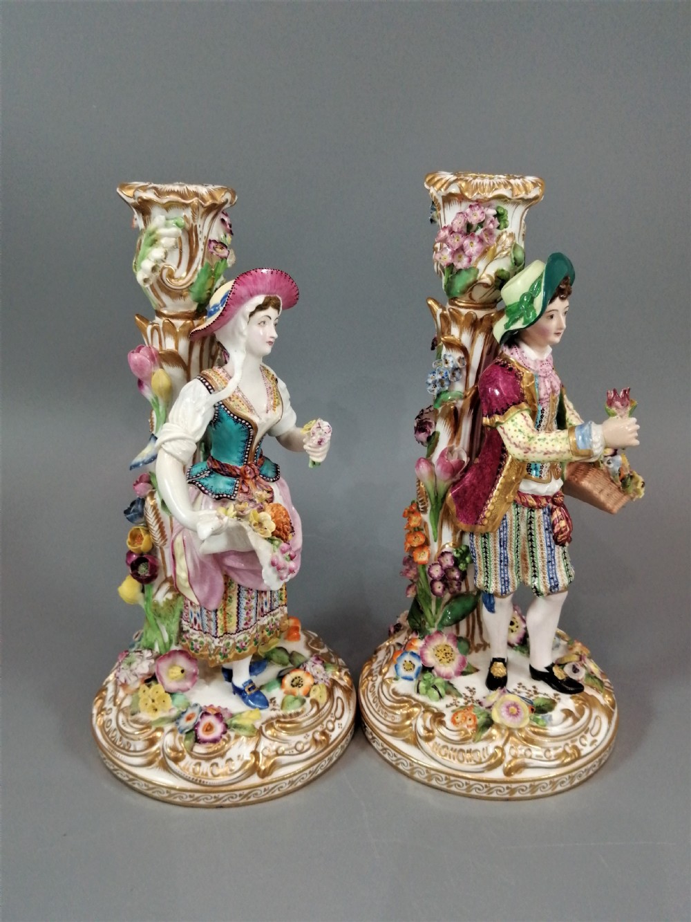 A pair of hand-painted Minton porcelain figural candlesticks featuring a male and female figure in colourful traditional dress with floral motifs and gilded scroll bases. View XVII