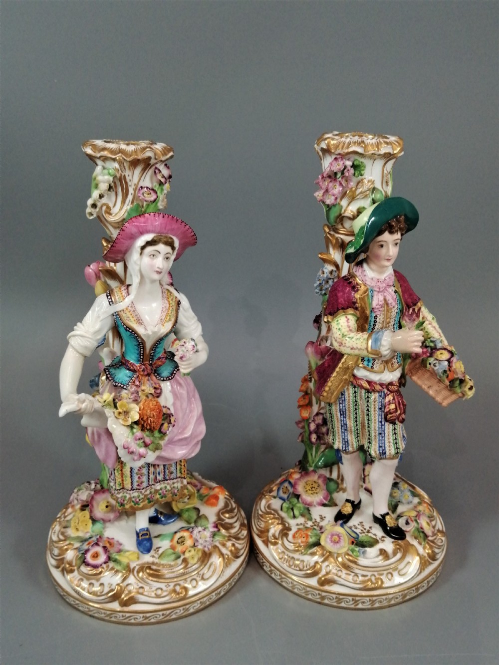 A pair of hand-painted Minton porcelain figural candlesticks featuring a male and female figure in colourful traditional dress with floral motifs and gilded scroll bases. View XVIII