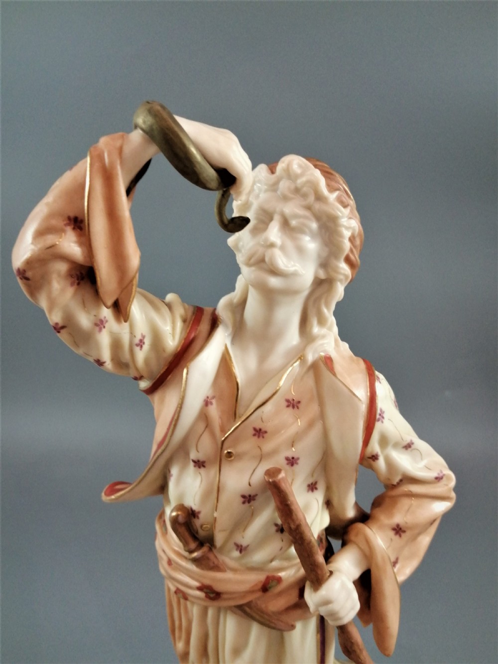 A nineteenth-century Royal Worcester porcelain figurine depicting a standing snake charmer holding a snake aloft beside a tree stump base. View VIII