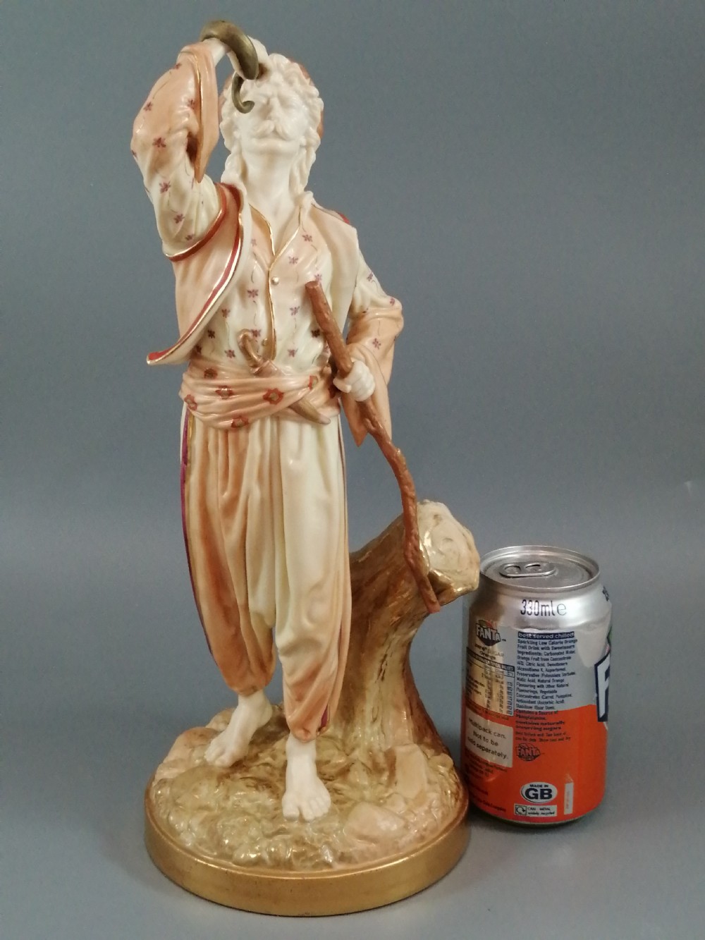 A nineteenth-century Royal Worcester porcelain figurine depicting a standing snake charmer holding a snake aloft beside a tree stump base. View X