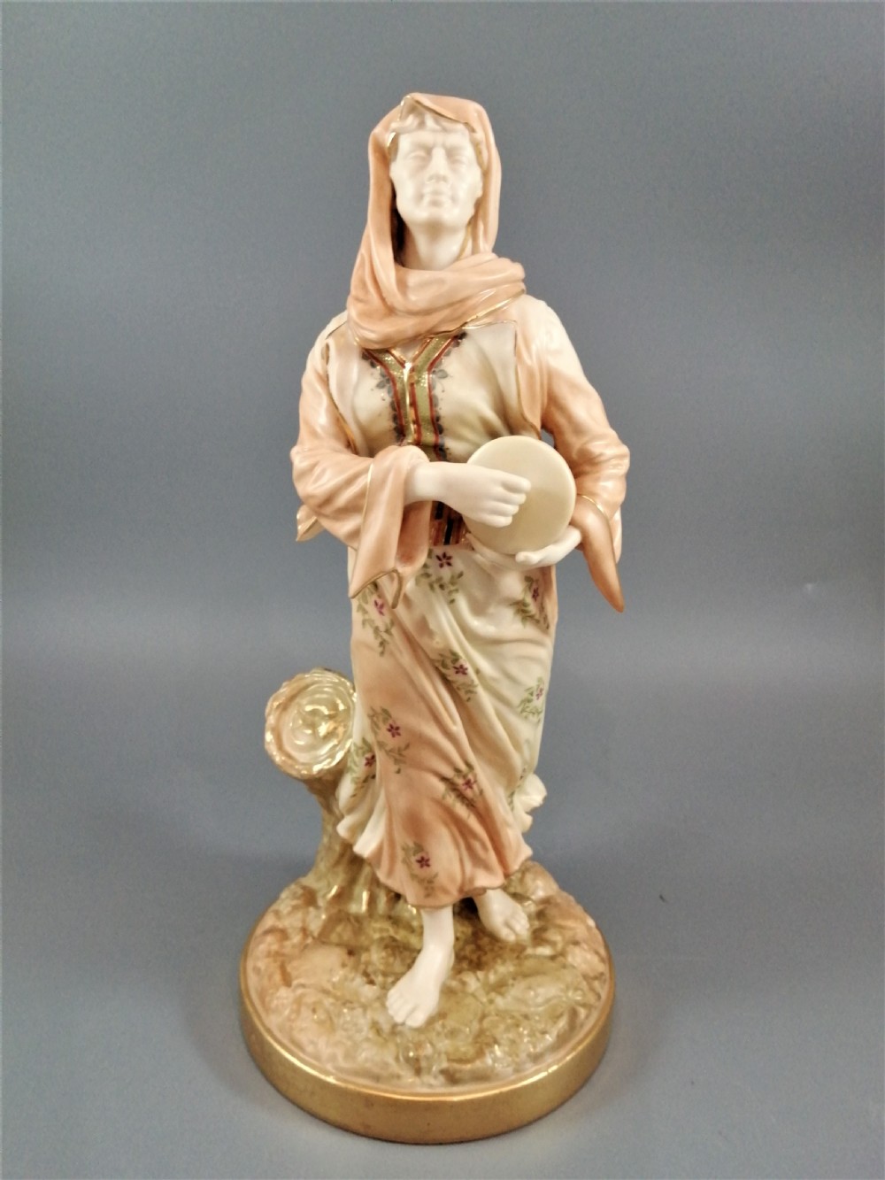 A late Victorian Royal Worcester porcelain figurine depicting a standing female musician in draped robes holding a hand drum.