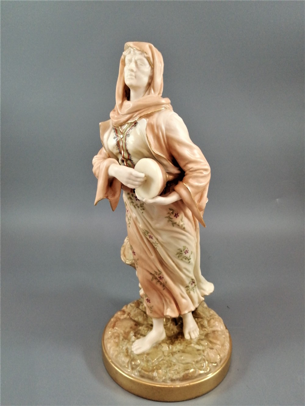 A late Victorian Royal Worcester porcelain figurine depicting a standing female musician in draped robes holding a hand drum. View II