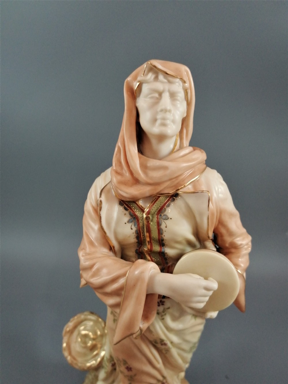 A late Victorian Royal Worcester porcelain figurine depicting a standing female musician in draped robes holding a hand drum. View IX