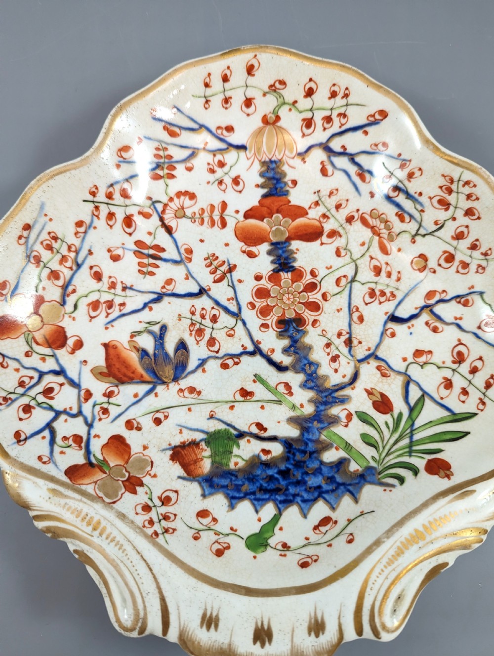 An antique shell-shaped porcelain plate featuring hand-painted Kakiemon-style motifs of two quails beneath flowering branches with gilt highlights. View III