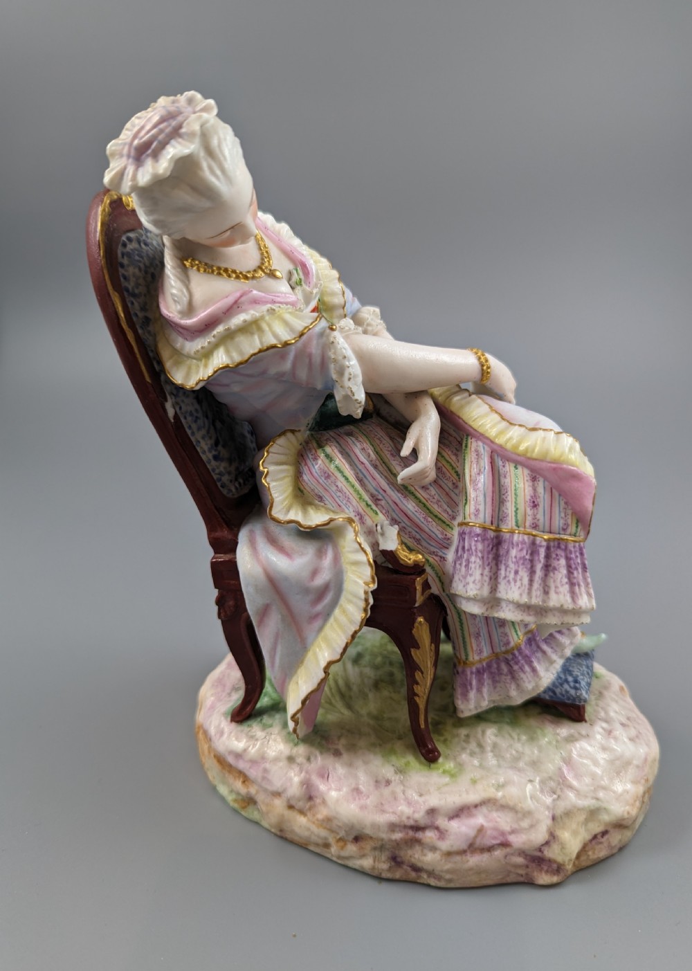 A 19th-century French biscuit porcelain figurine depicting a sleeping lady seated in a chair with pastel pink drapery and gold accents. View V