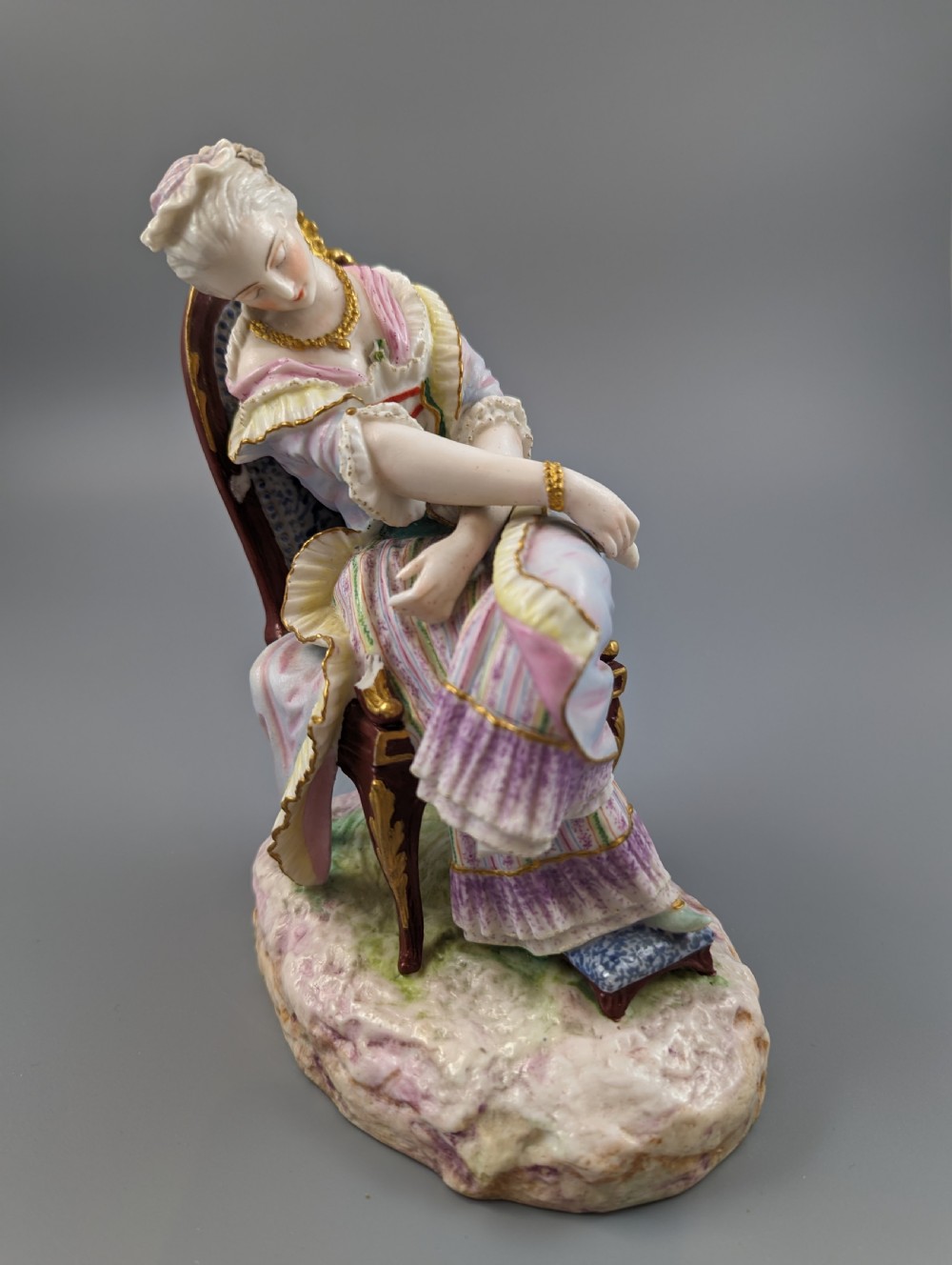 A 19th-century French biscuit porcelain figurine depicting a sleeping lady seated in a chair with pastel pink drapery and gold accents. View VIII