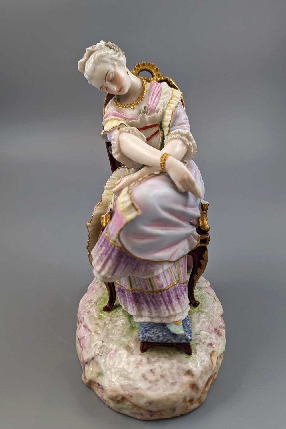 A 19th-century French biscuit porcelain figurine depicting a sleeping lady seated in a chair with pastel pink drapery and gold accents. View IX