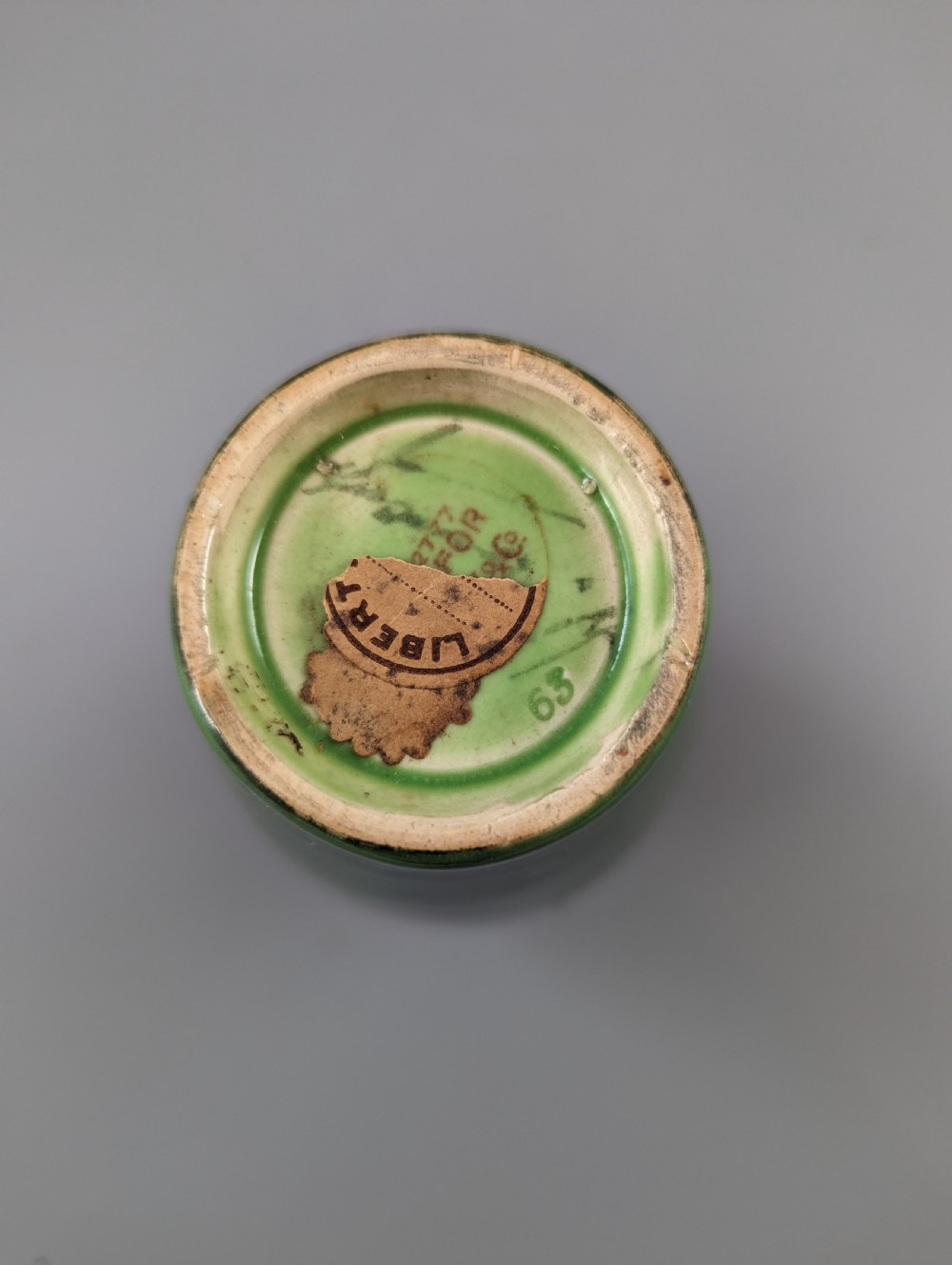 A green glazed ceramic vase with a flared neck and a central circular slip-trailed medallion featuring a stylized motif in blue, green, and cream. View IX