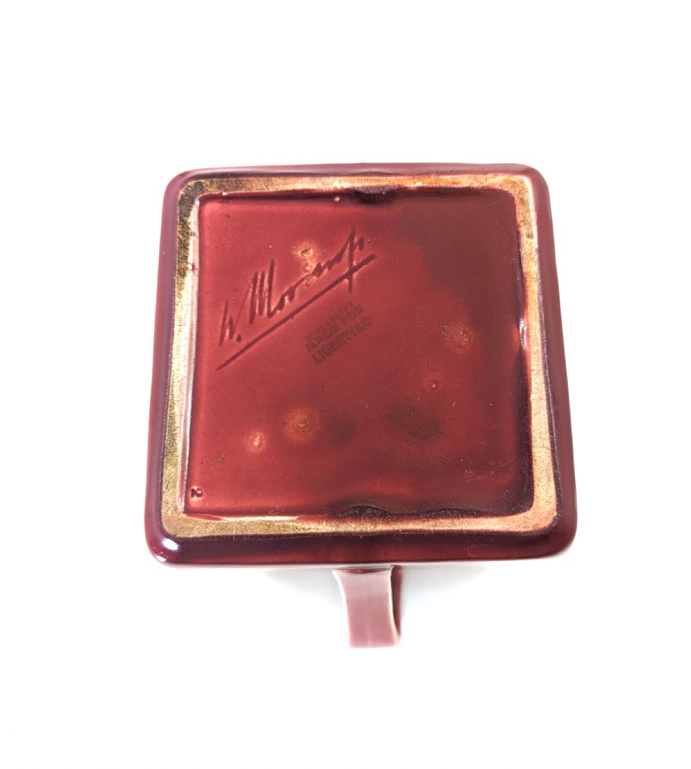 A square red glazed ceramic vessel with twin loop handles and a central circular motif on the front surface. View IX