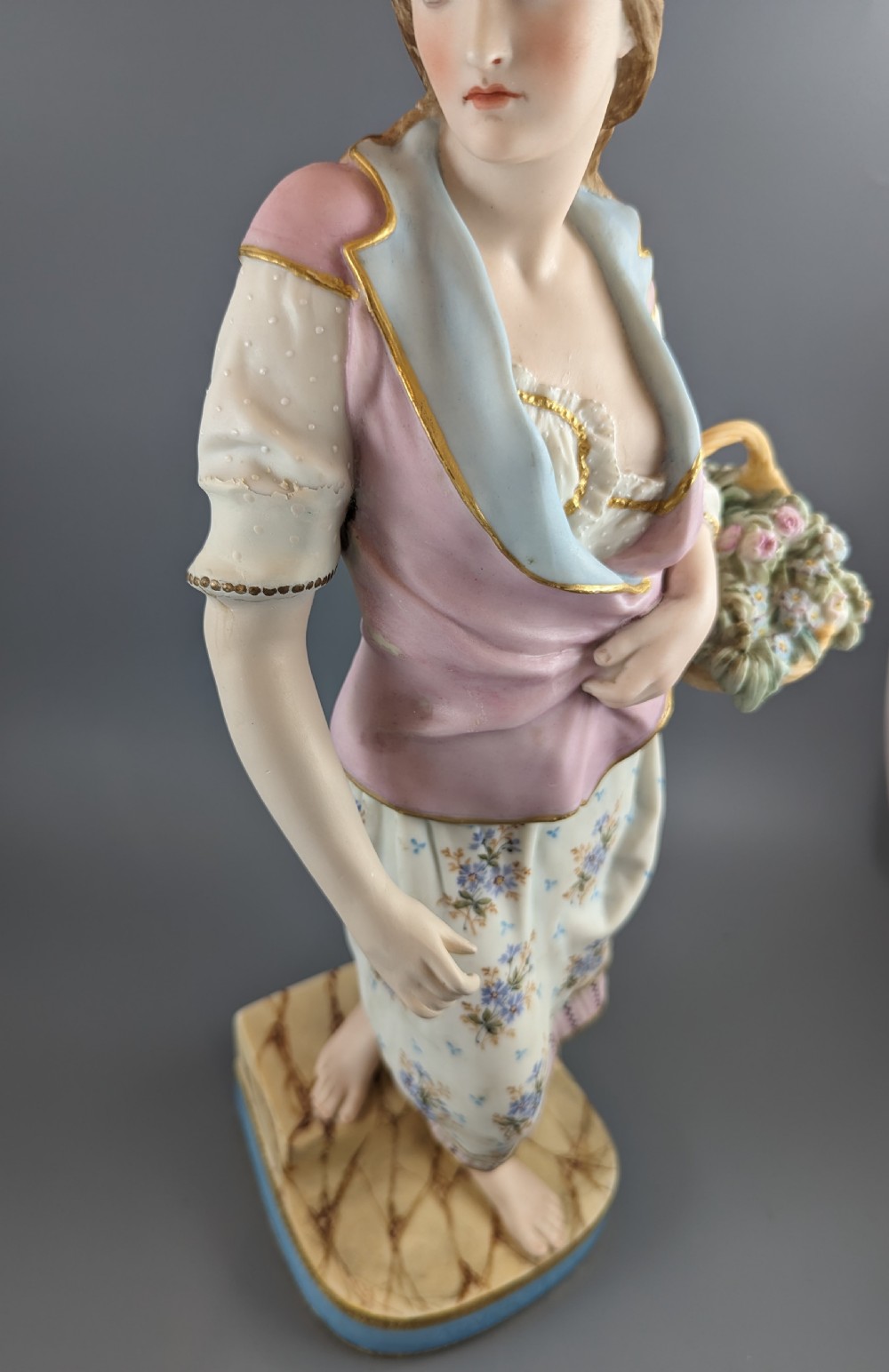 A Victorian coloured Parian porcelain figure depicting a draped female figure holding a basket of flowers on a faux-marble painted base. View IX