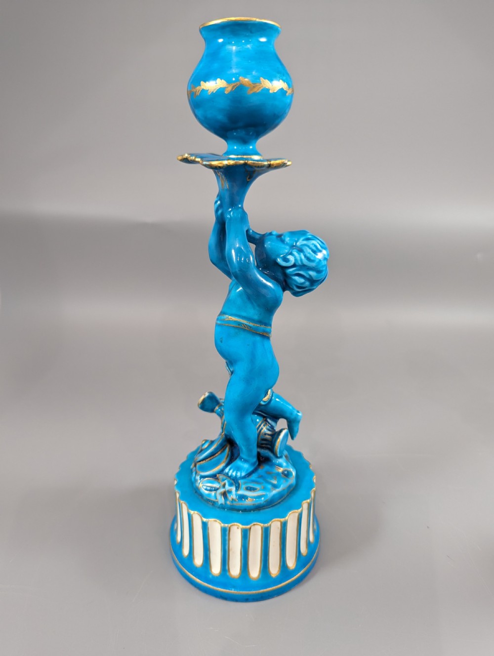 A pair of turquoise blue glazed porcelain candlesticks shaped as cherubs supporting urn sockets on fluted bases with gold trim. View II