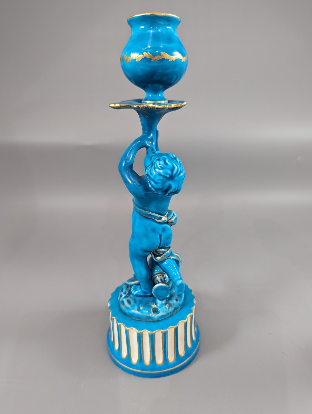 A pair of turquoise blue glazed porcelain candlesticks shaped as cherubs supporting urn sockets on fluted bases with gold trim. View III