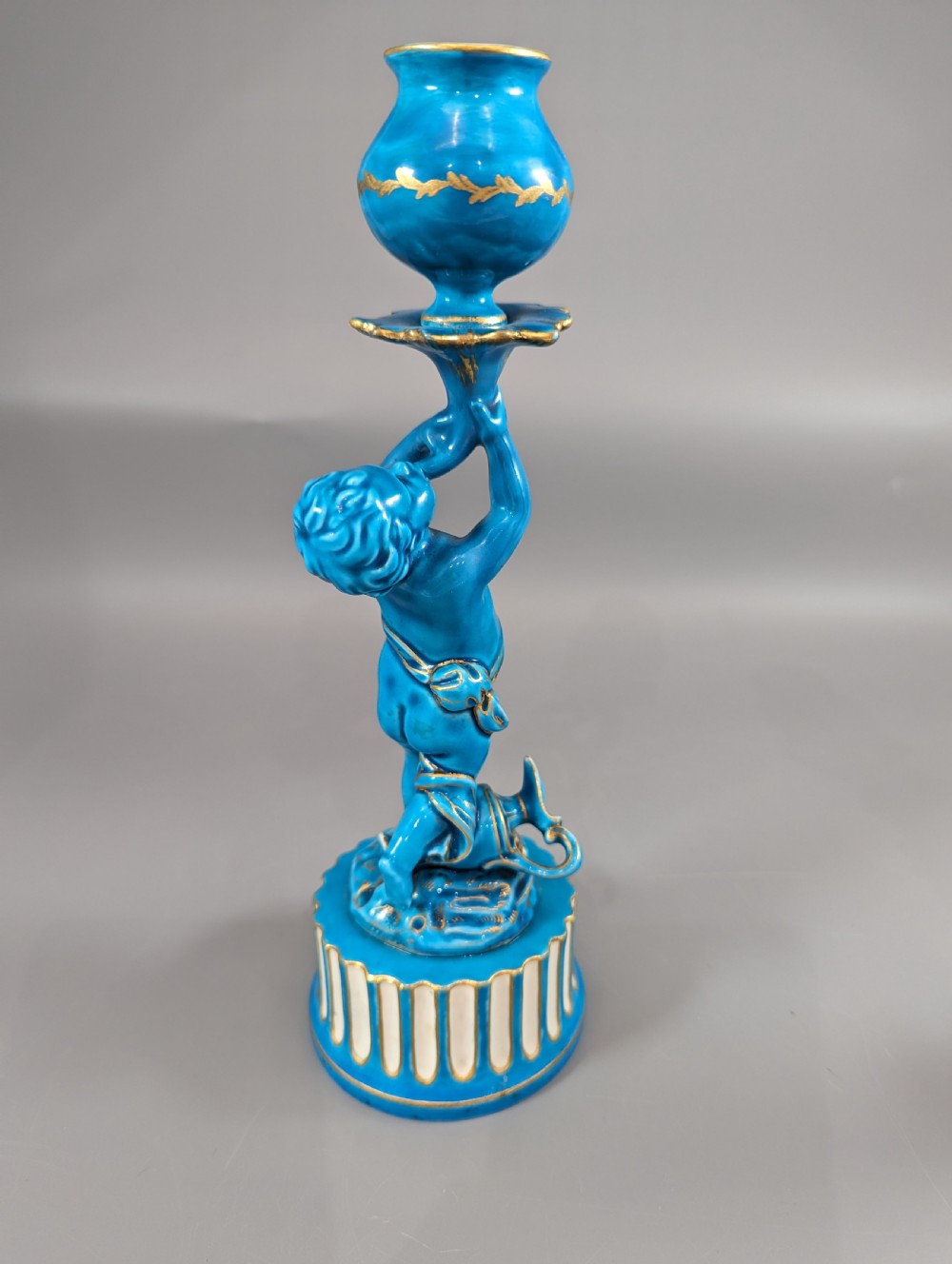 A pair of turquoise blue glazed porcelain candlesticks shaped as cherubs supporting urn sockets on fluted bases with gold trim. View IV